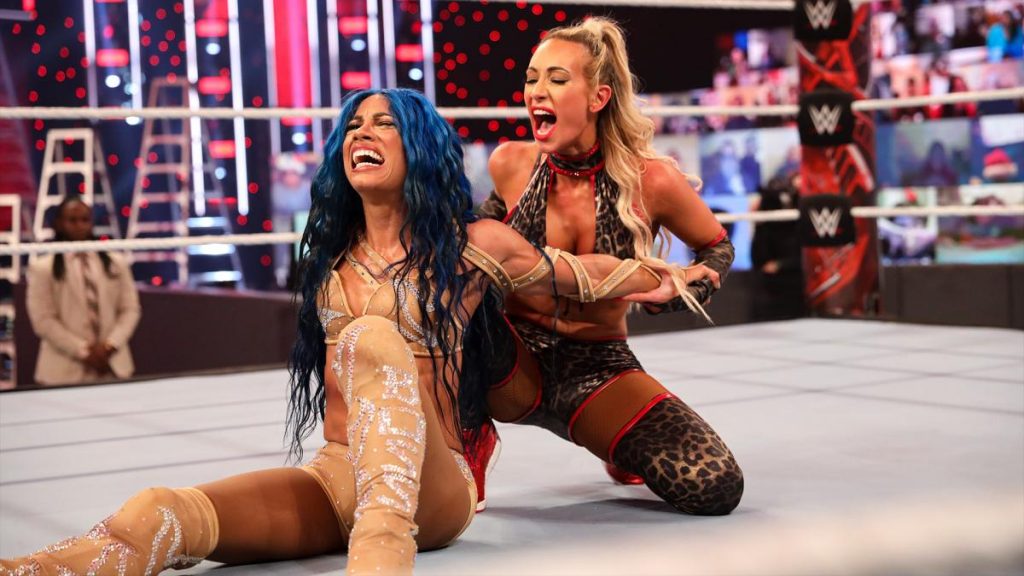 Carmella and Sasha Banks on WWE with Reginald in the background. (WWE)